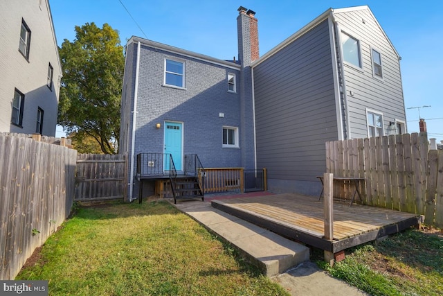 back of house featuring a deck, a fenced backyard, brick siding, a yard, and a chimney