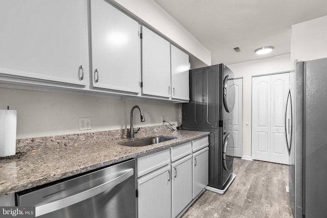 kitchen with visible vents, a sink, stainless steel appliances, light wood-style floors, and stacked washer / drying machine