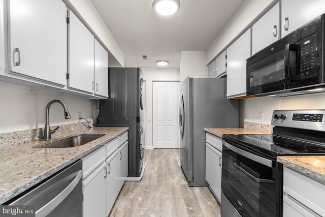 kitchen featuring light stone countertops, a sink, stainless steel appliances, stacked washer and dryer, and light wood-type flooring