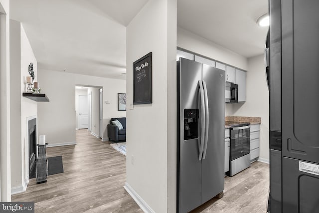 kitchen featuring stainless steel appliances, a fireplace with flush hearth, baseboards, and light wood-style flooring