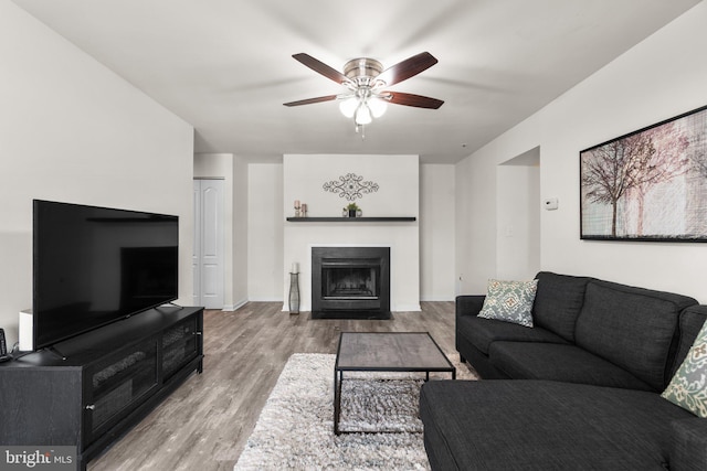 living area with a ceiling fan, a fireplace with flush hearth, wood finished floors, and baseboards