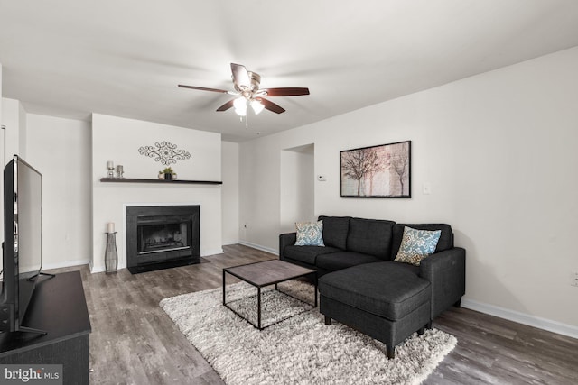 living room featuring ceiling fan, baseboards, a fireplace with flush hearth, and wood finished floors