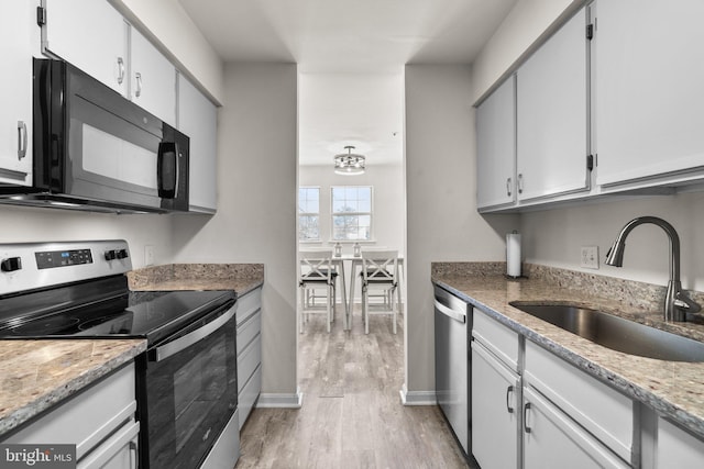 kitchen featuring light stone counters, light wood-style flooring, appliances with stainless steel finishes, white cabinets, and a sink