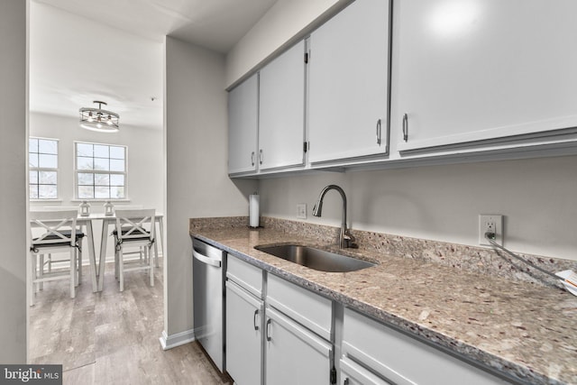 kitchen featuring baseboards, light stone countertops, dishwasher, light wood-style floors, and a sink