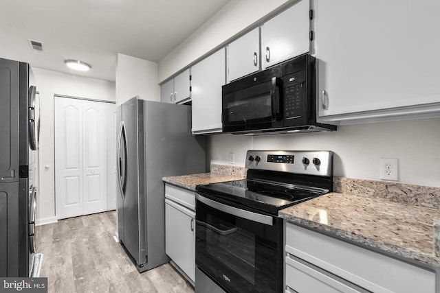 kitchen with light stone countertops, visible vents, stacked washer / drying machine, appliances with stainless steel finishes, and light wood-type flooring