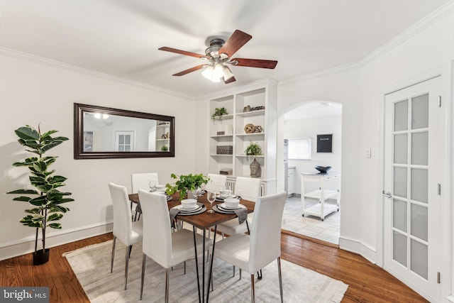 dining area with baseboards, arched walkways, wood finished floors, and ornamental molding