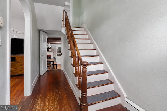 stairway featuring arched walkways, wood finished floors, baseboards, and a baseboard radiator