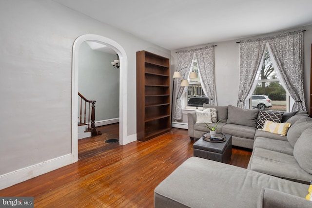 living area featuring baseboards, stairway, baseboard heating, hardwood / wood-style flooring, and arched walkways