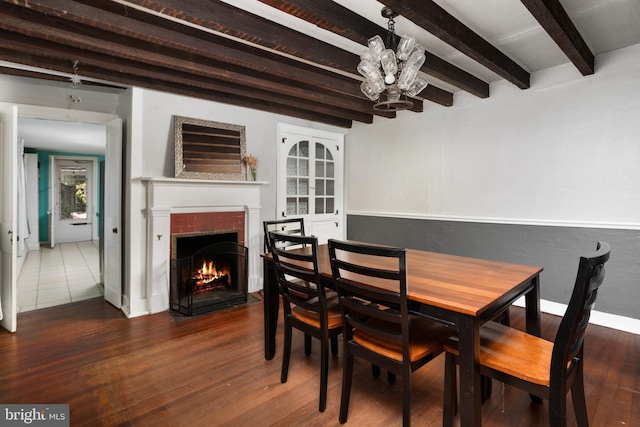 dining space with beam ceiling, a fireplace with flush hearth, wood finished floors, and a chandelier