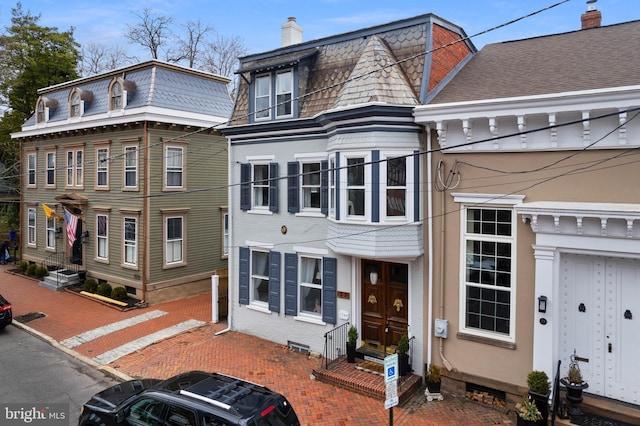 view of front facade featuring brick siding, mansard roof, and a chimney