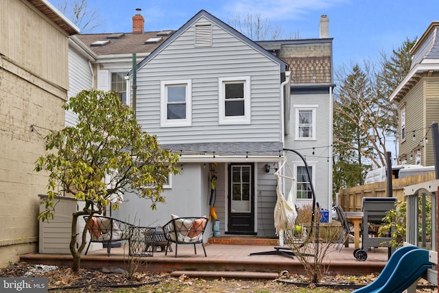 back of property featuring fence, roof with shingles, a chimney, and a patio area