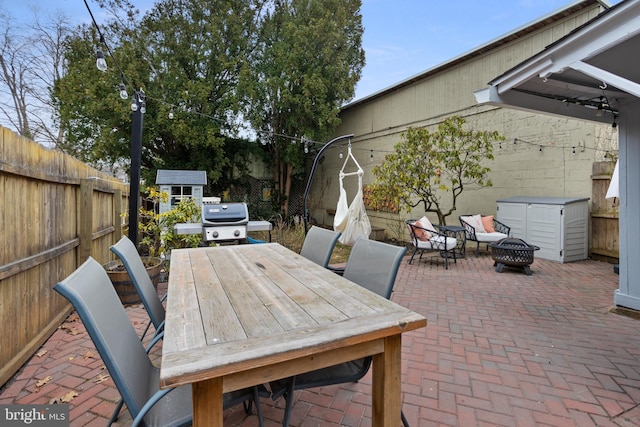 view of patio with a fire pit, a shed, a fenced backyard, an outdoor structure, and outdoor dining space