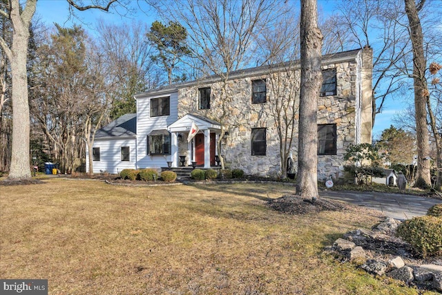 colonial-style house featuring stone siding and a front lawn