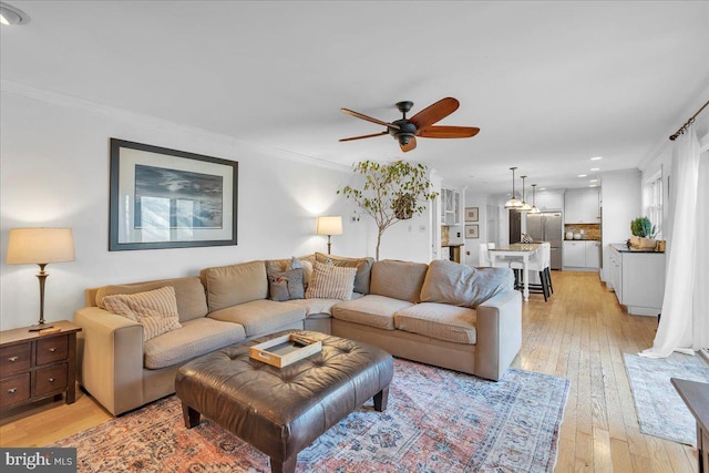 living area with light wood-style floors, ceiling fan, and crown molding