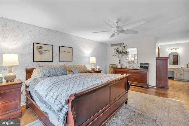 bedroom with light wood-style floors, visible vents, a ceiling fan, and ensuite bathroom