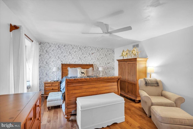 bedroom with wallpapered walls, an accent wall, visible vents, and wood finished floors