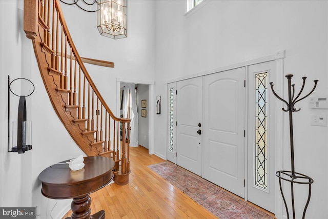 foyer featuring a towering ceiling, wood-type flooring, stairs, and a chandelier