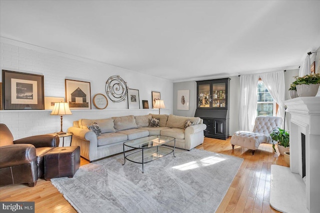 living area featuring brick wall, light wood-style flooring, a fireplace, and ornamental molding