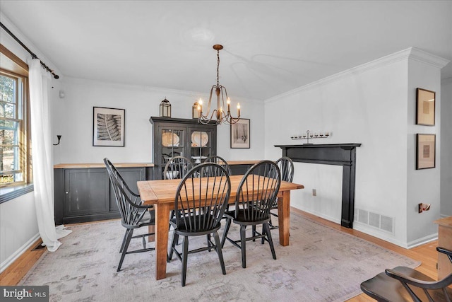 dining room featuring crown molding, light wood-type flooring, visible vents, and an inviting chandelier