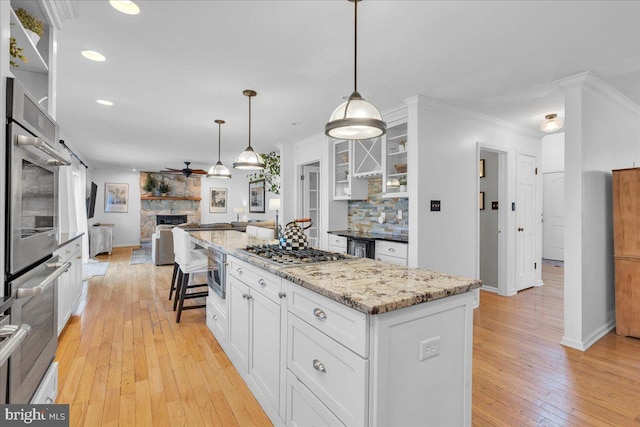 kitchen featuring a fireplace, appliances with stainless steel finishes, ornamental molding, open floor plan, and white cabinetry