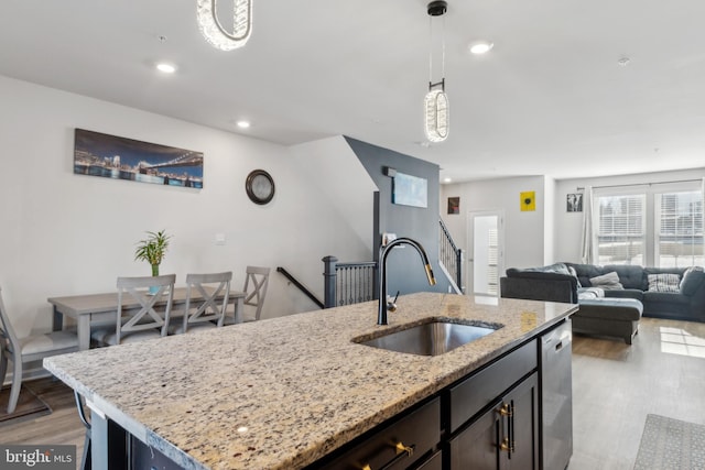 kitchen with a center island with sink, open floor plan, hanging light fixtures, light stone countertops, and a sink