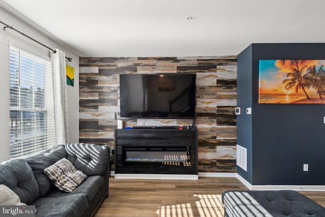 living area featuring an accent wall, wood finished floors, visible vents, and baseboards