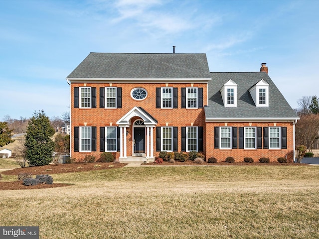 view of front of house with brick siding, roof with shingles, and a front yard