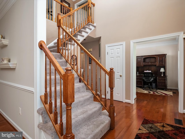 staircase with crown molding, visible vents, a towering ceiling, hardwood / wood-style floors, and baseboards