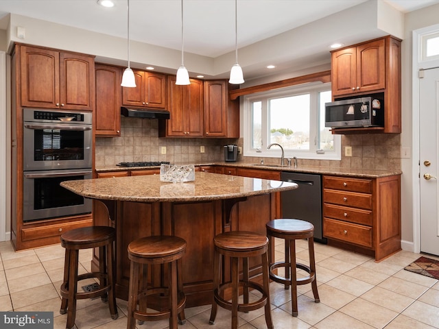 kitchen with decorative backsplash, light stone counters, appliances with stainless steel finishes, a center island, and a sink