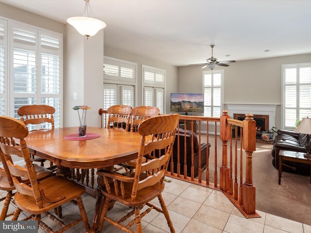 dining room with a ceiling fan, light carpet, a fireplace, and light tile patterned floors