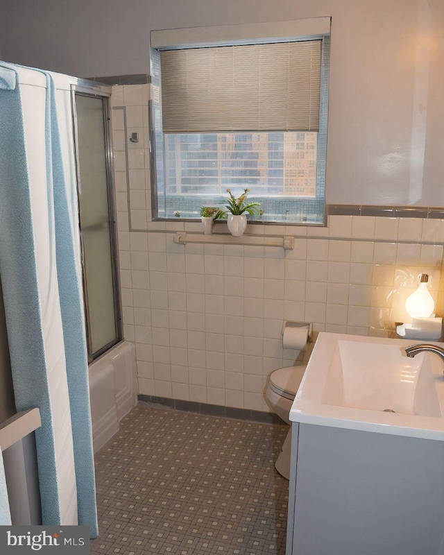 bathroom featuring toilet, enclosed tub / shower combo, tile patterned flooring, vanity, and tile walls