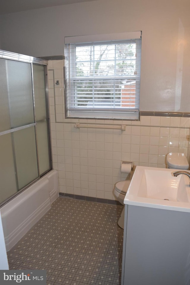 full bath with bath / shower combo with glass door, toilet, tile patterned flooring, vanity, and tile walls