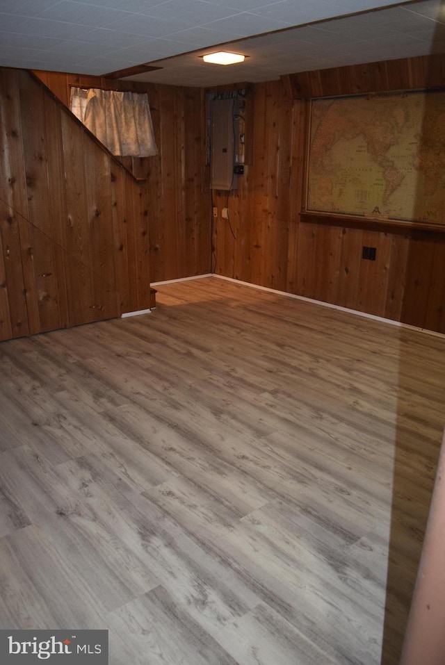 finished below grade area with electric panel, wooden walls, and wood finished floors