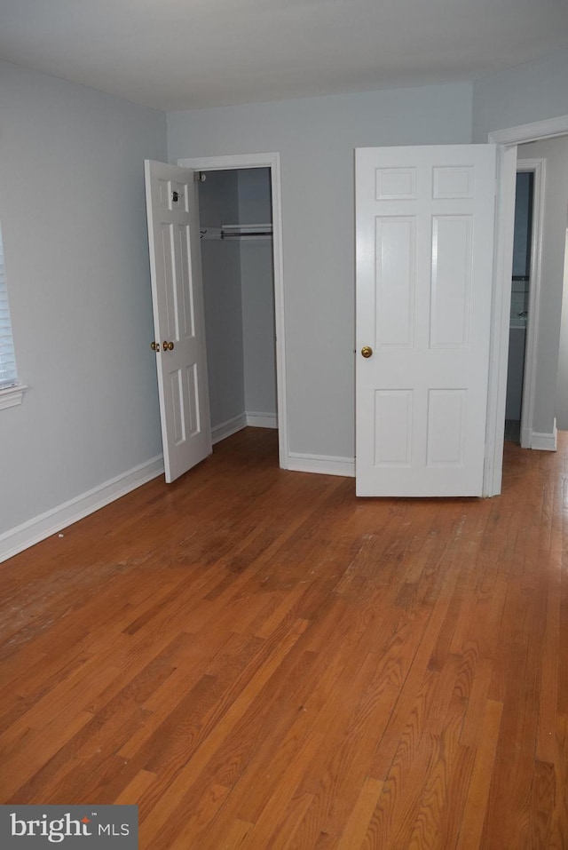 unfurnished bedroom with a closet, wood finished floors, and baseboards