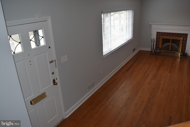 foyer entrance featuring visible vents, a fireplace, baseboards, and wood finished floors