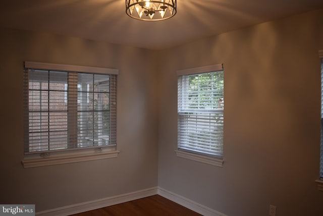 empty room with a notable chandelier, wood finished floors, and baseboards