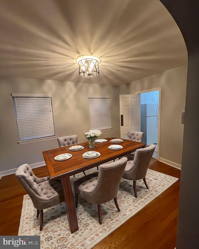 dining space with baseboards, arched walkways, and wood finished floors