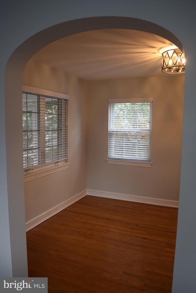 empty room featuring baseboards, arched walkways, and wood finished floors