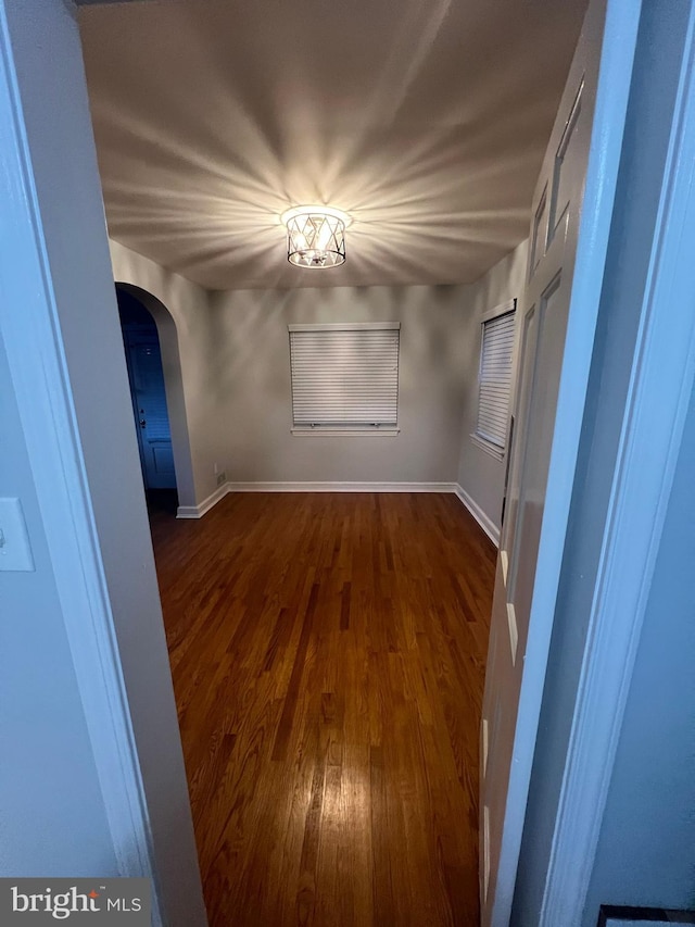 empty room featuring arched walkways, dark wood-type flooring, and baseboards