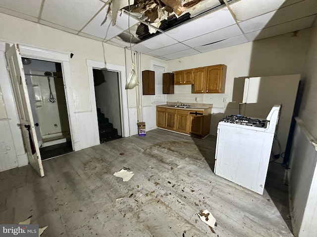 kitchen with a paneled ceiling, brown cabinets, a sink, and white gas range