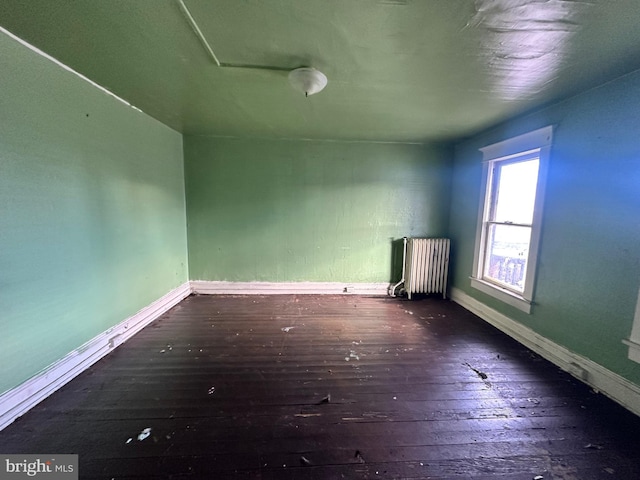 empty room featuring hardwood / wood-style flooring, radiator heating unit, and baseboards