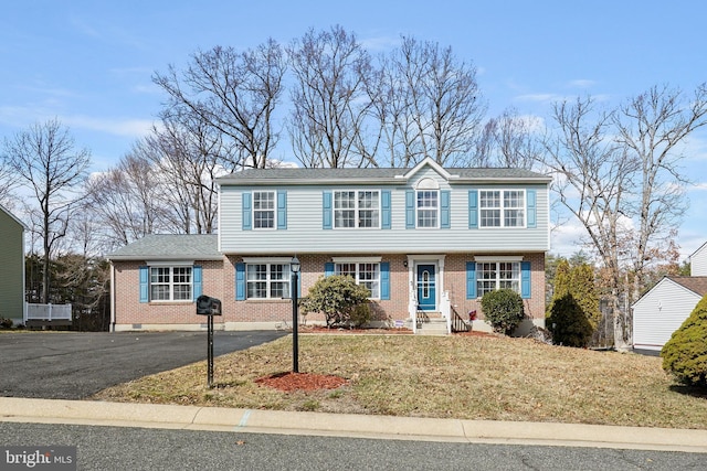 colonial inspired home featuring aphalt driveway, brick siding, and a front lawn