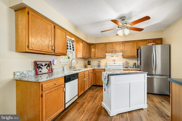 kitchen with brown cabinets, a sink, wood finished floors, white appliances, and under cabinet range hood