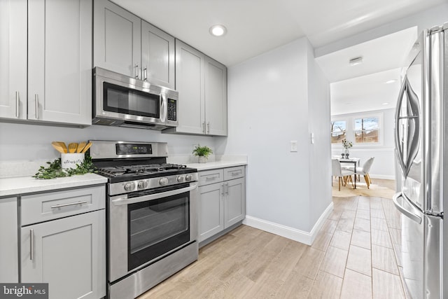 kitchen featuring light countertops, light wood-style flooring, gray cabinetry, appliances with stainless steel finishes, and baseboards