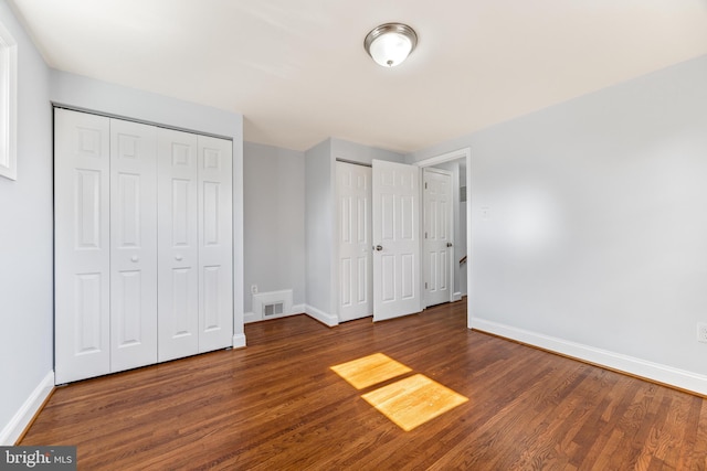 unfurnished bedroom featuring baseboards, wood finished floors, visible vents, and multiple closets