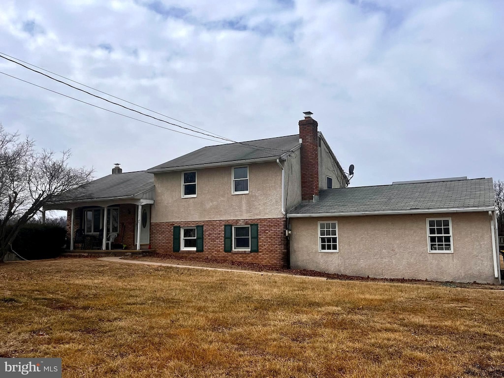 exterior space featuring a yard, brick siding, a chimney, and stucco siding