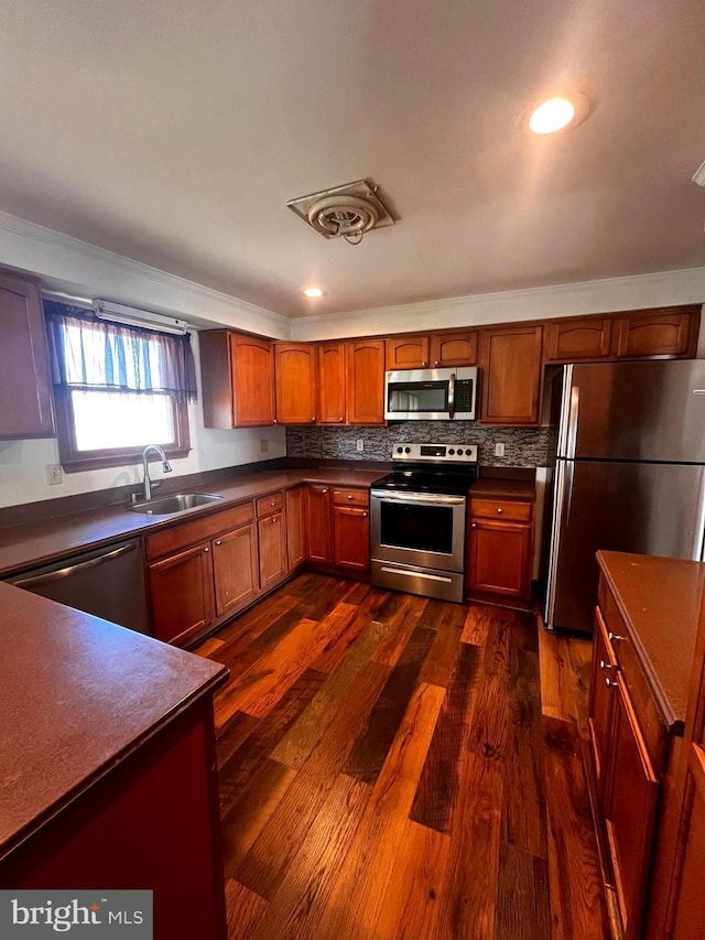 kitchen with stainless steel appliances, dark wood-style flooring, a sink, tasteful backsplash, and dark countertops