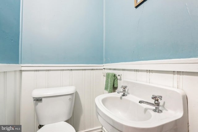 half bathroom featuring wainscoting, a sink, and toilet