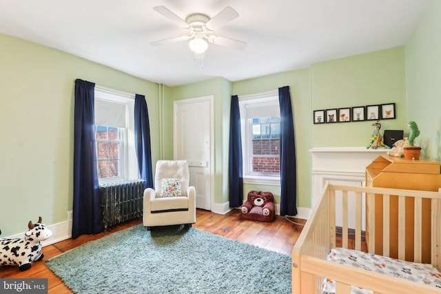 bedroom with a nursery area, multiple windows, baseboards, and wood finished floors