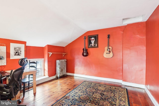 home office featuring vaulted ceiling, hardwood / wood-style floors, baseboards, and radiator